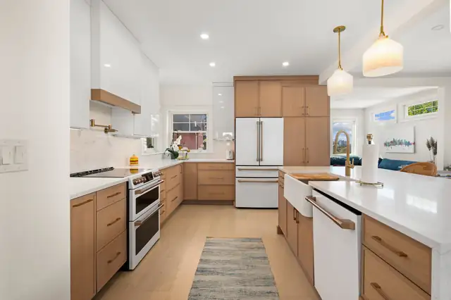 Kitchen by Halco with natural wood cabinets, a long white island, white appliances and glass pendant lights