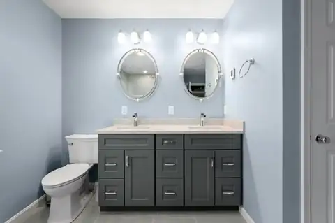 North Reading, MA primary bathroom with a charcoal double vanity, white quartz top, oval mirrors and light blue walls