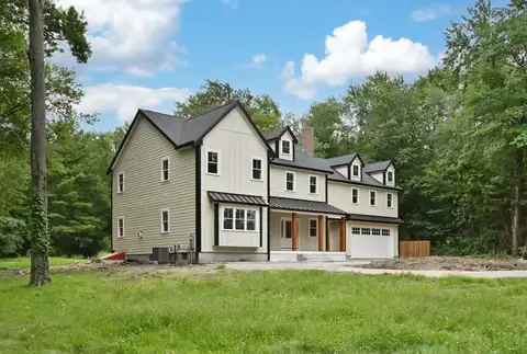 Middleton, MA home addition with sage siding, a dark roof, a covered front porch and an attached garage