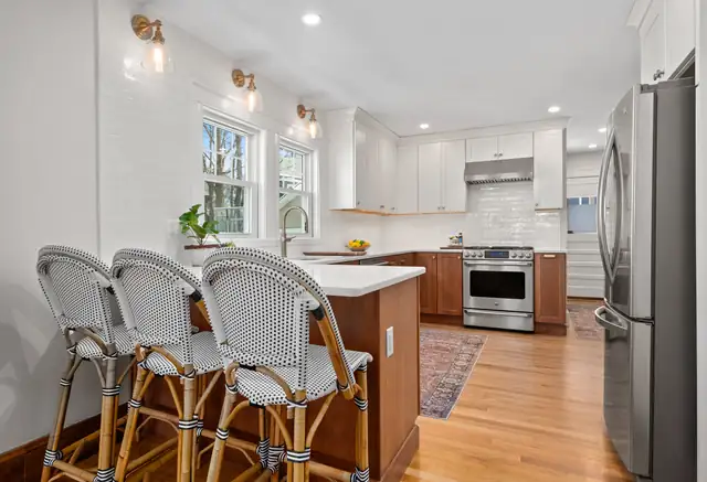 Melrose kitchen with white cabinets, a stained wood island with woven counter stools and brass sconces
