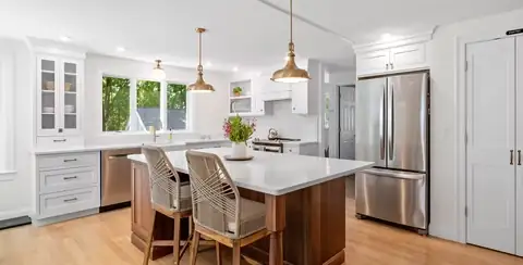 Wakefield, MA kitchen with a walnut island, white perimeter cabinets, rattan counter stools and brass pendant lights