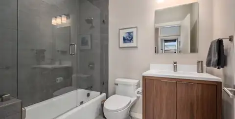 Boston South End condo bathroom with dark gray tile tub and shower, glass panel and a walnut floating vanity