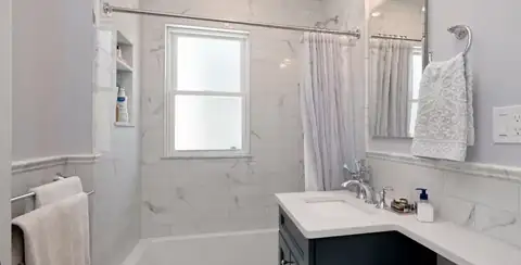 Cambridge, MA bathroom with white marble-look wall tile, a tub with curtain rod and a navy vanity with white top