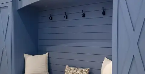 Boxford, MA custom mudroom with a blue shiplap bench nook, black coat hooks and X-panel cabinet doors